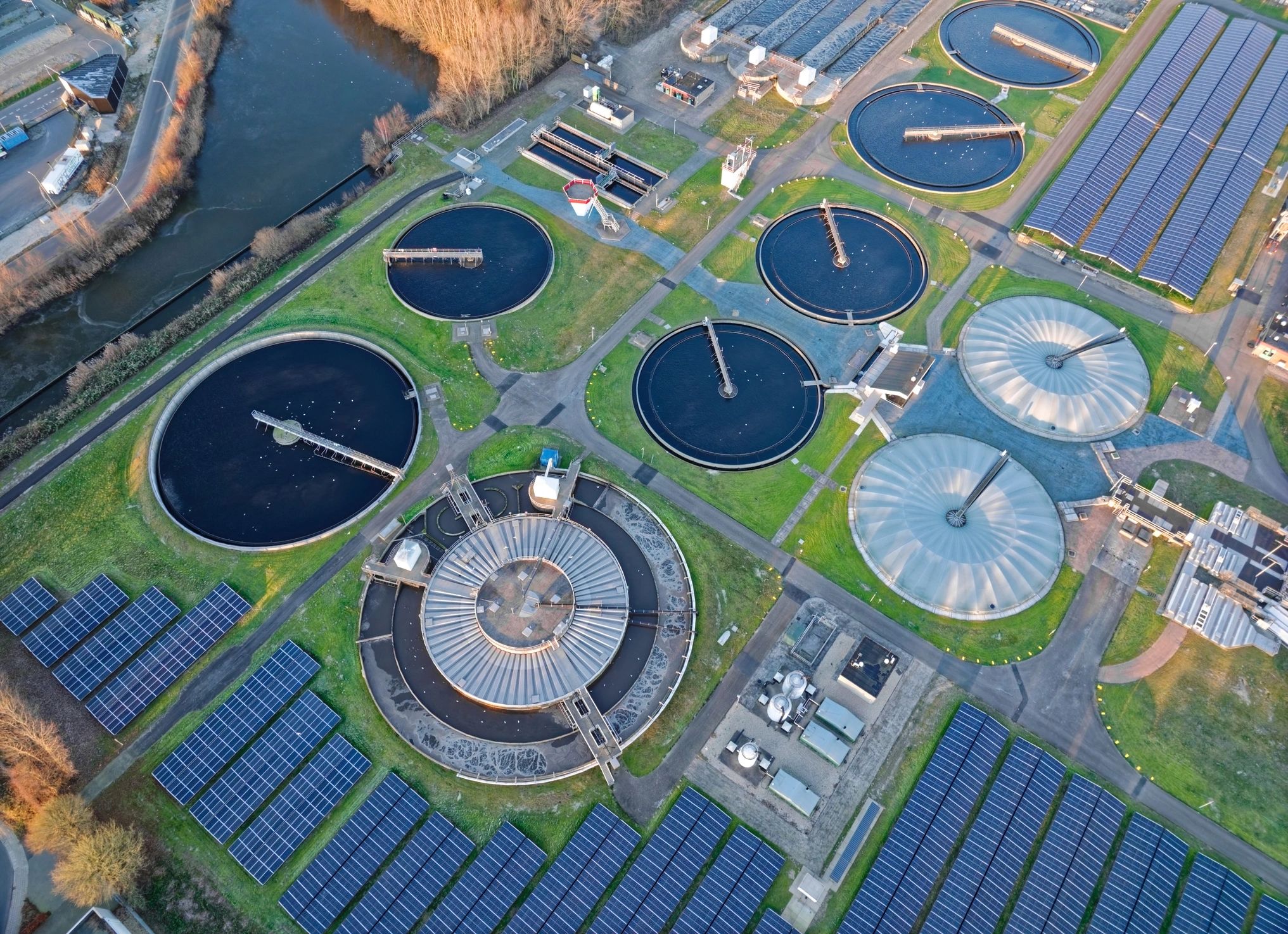 Modern wastewater treatment plant with circular clarifier basins and solar panels